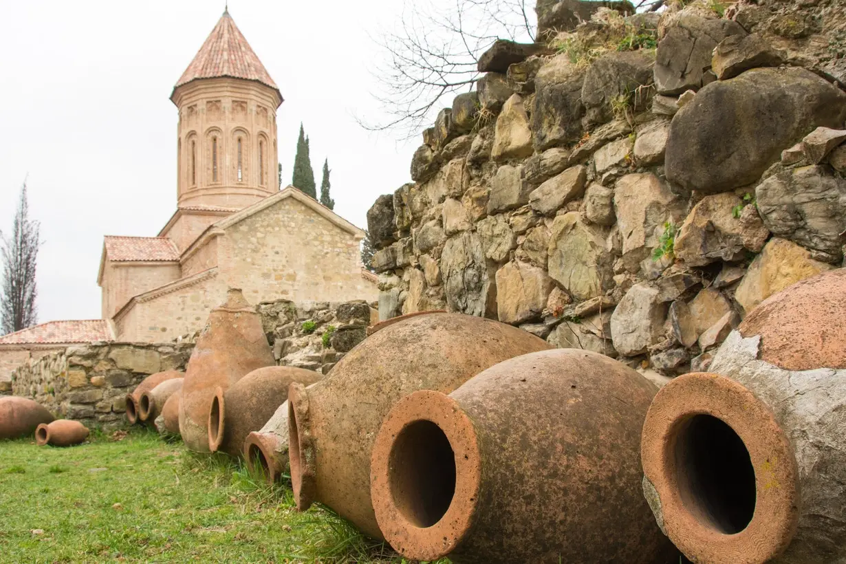 Qvevri di terracotta allineati sul prato davanti a una chiesa georgiana in pietra